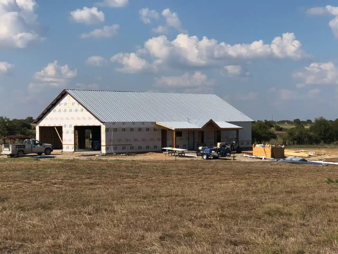 White barndominium under construction with house wrap, a metal roof and open garage bays
